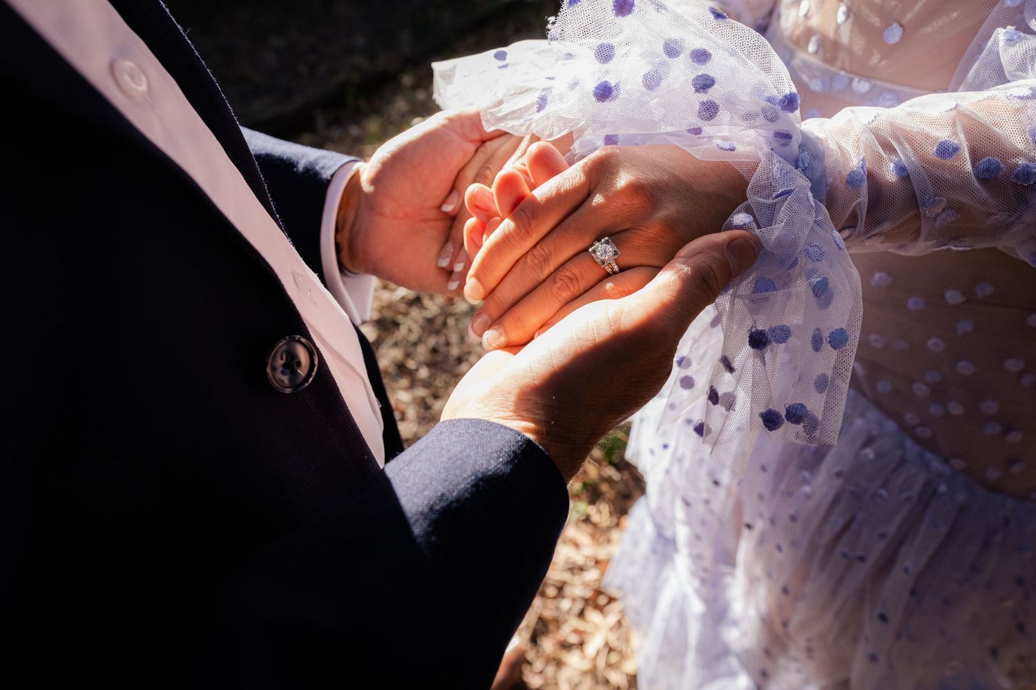 Close-up shot of hands exchanging wedding rings during a ceremony against a textured background.