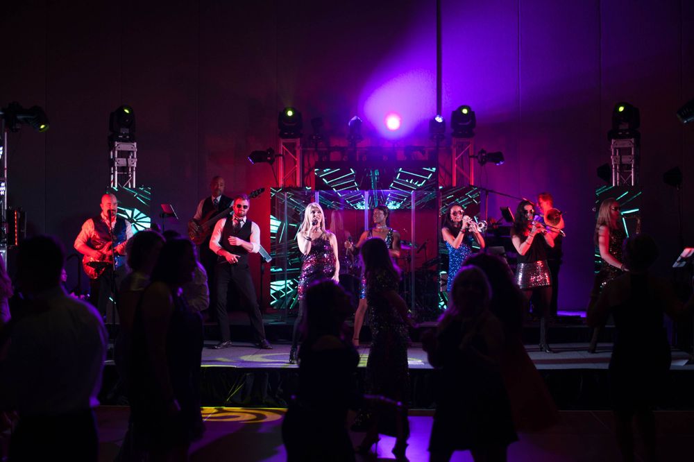 Band performing on stage with purple lighting and silhouetted crowd.