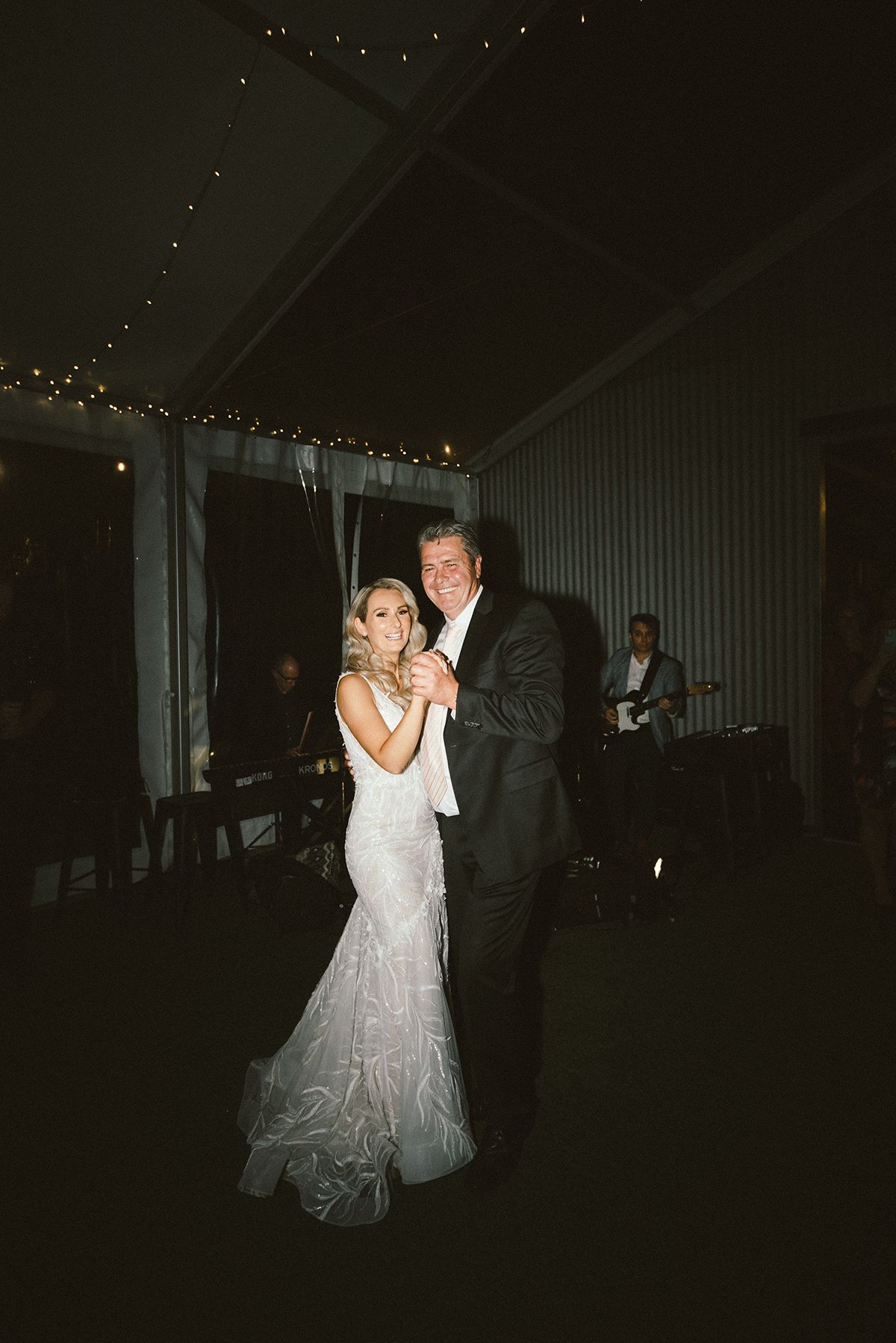 A couple dancing in dim lighting with twinkling lights overhead at a reception venue.