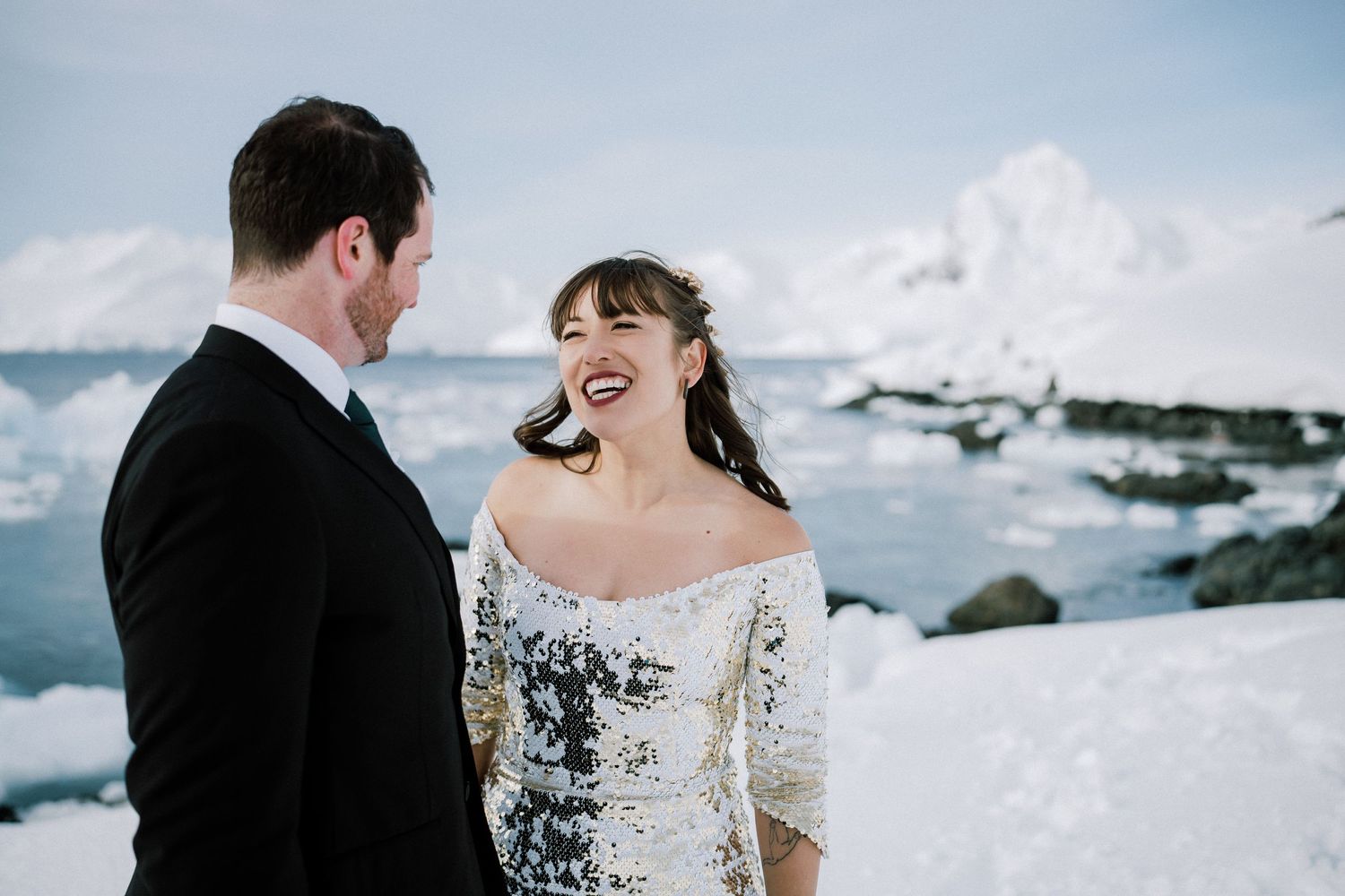 A couple sharing a joyful moment against a snowy Antarctic landscape with glaciers.