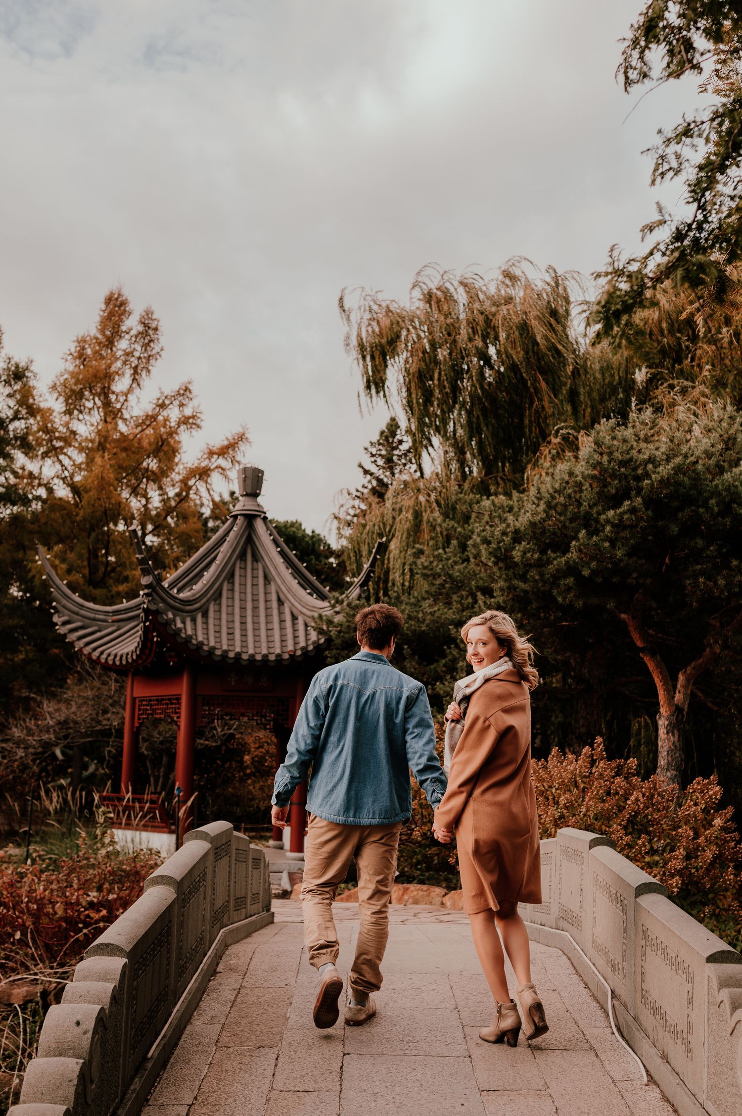Couple walking across arched bridge near Asian pagoda during autumn.