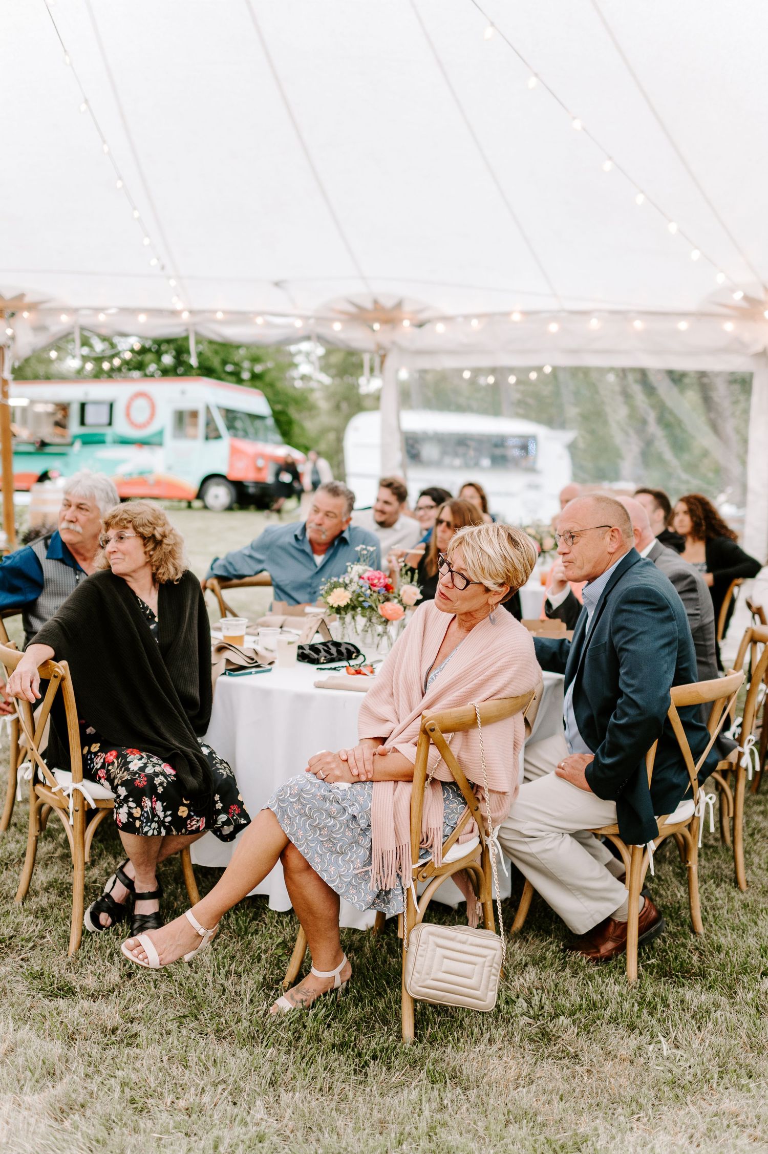 Wedding guests enjoying the reception at round tables under an airy white tent.
