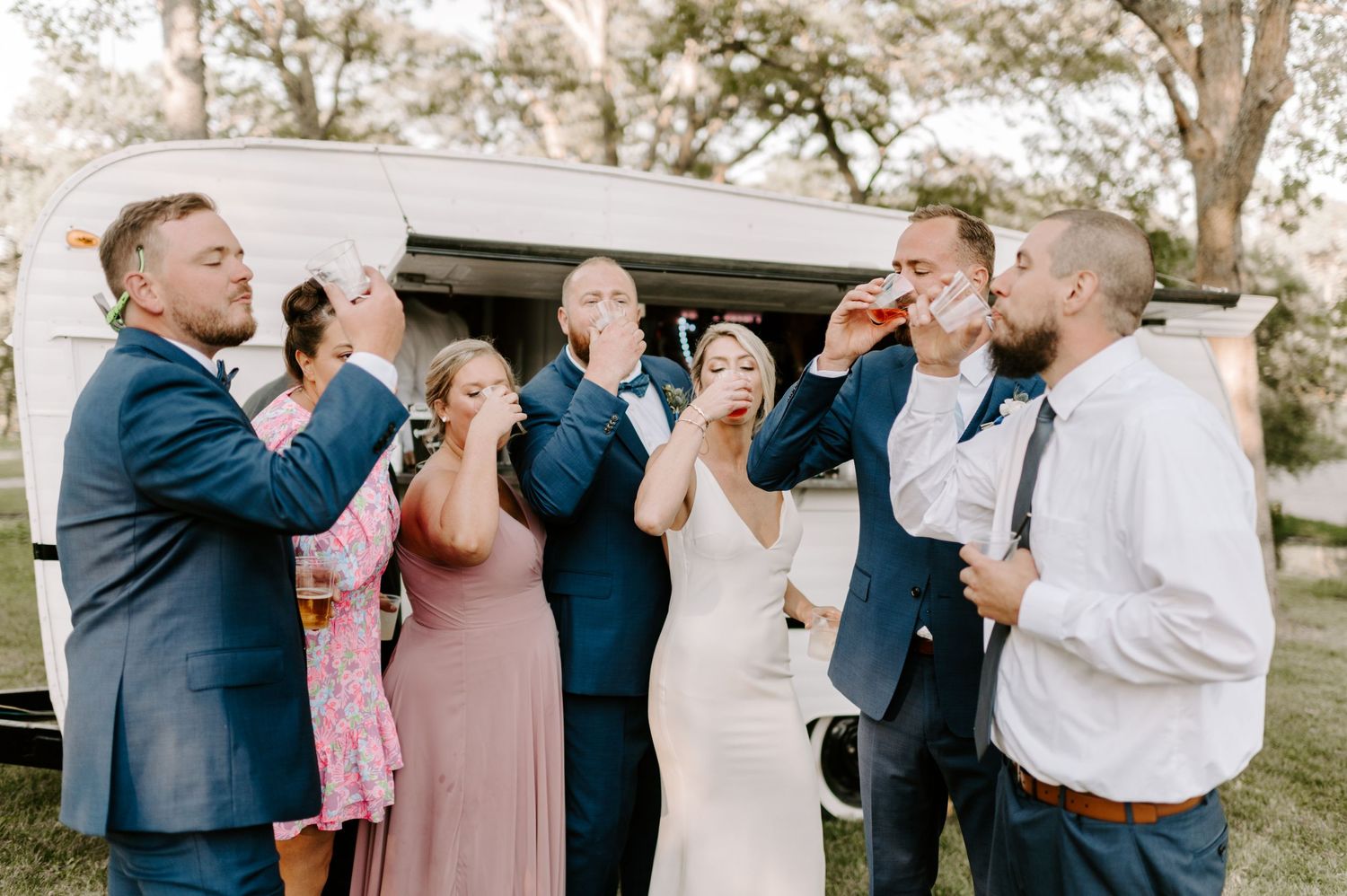 Wedding guests laugh and celebrate during an outdoor reception under a white tent.