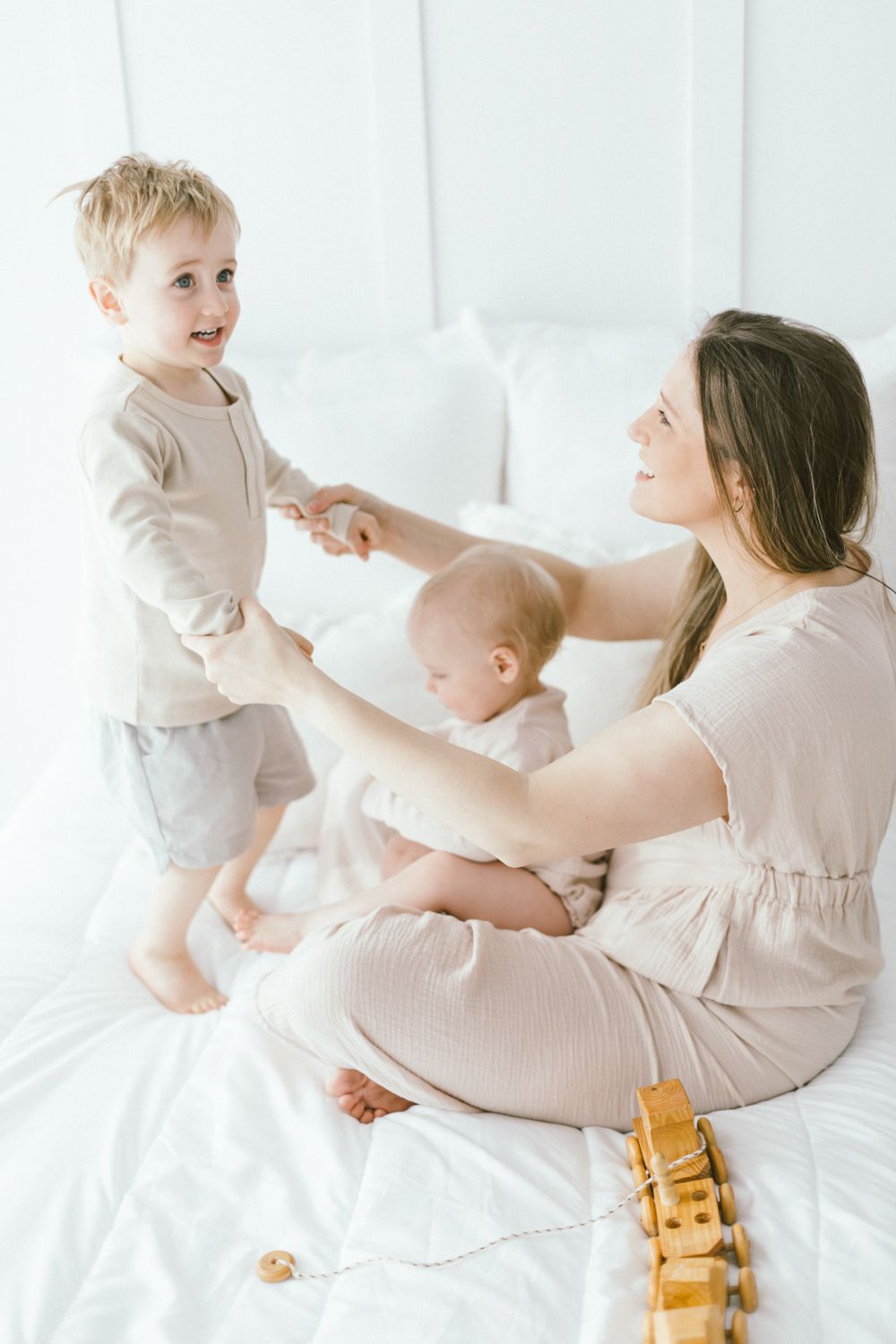 Family enjoying playful moments together on white bedding with wooden toys nearby.