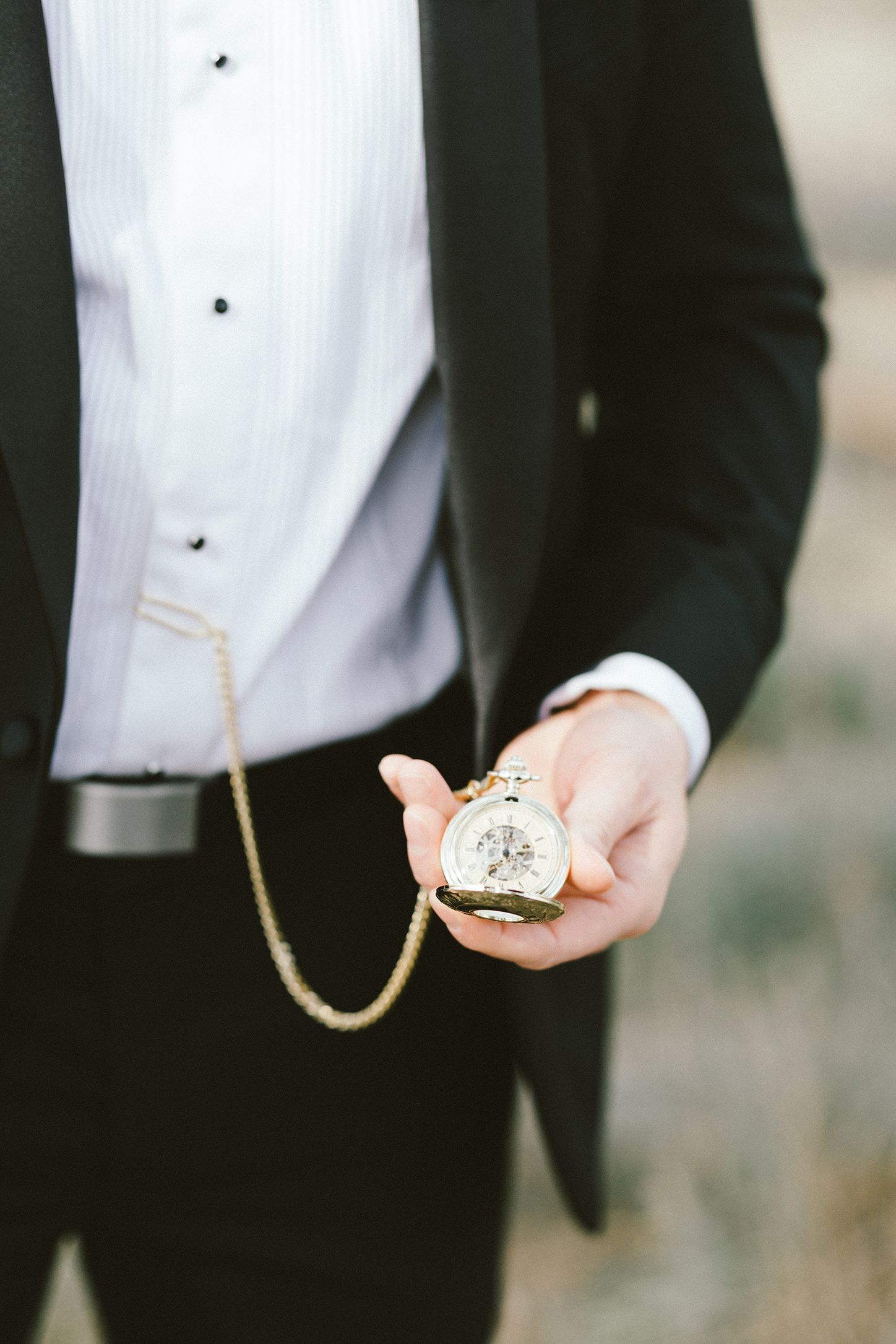 Close up of hands holding vintage pocket watch with chain against formal suit.