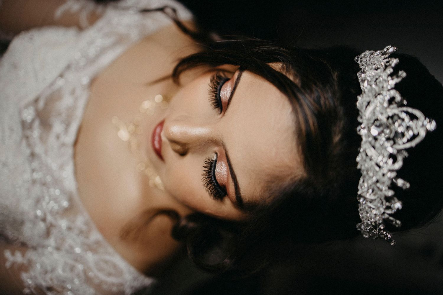 Close-up bridal portrait showing elegant lace veil and delicate tiara against dark background.