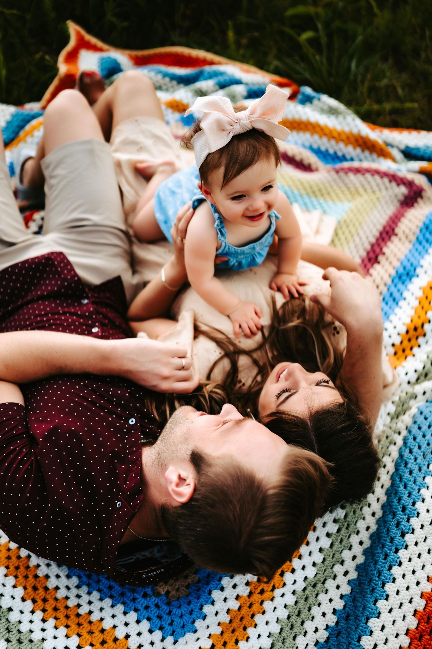 Family lying on a colorful crocheted blanket outdoors, enjoying quality time together.
