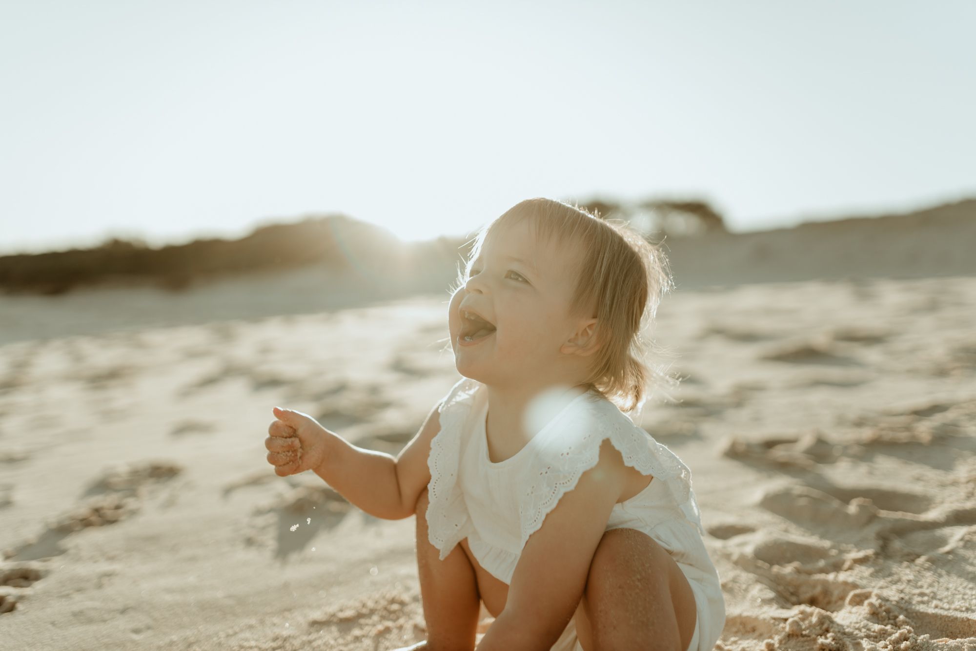 A small child playing in the sand at the beach during sunset.