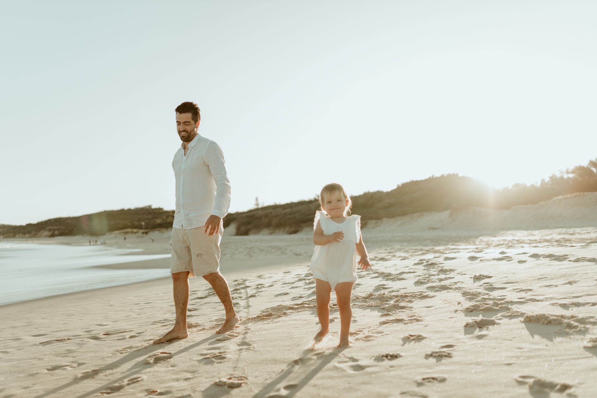 A parent and child walking together on the beach leaving footprints in the sand at sunset.