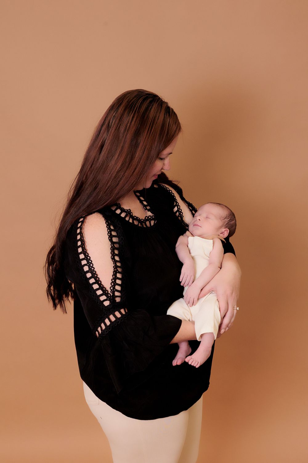 Mother in black sweater holding newborn baby against neutral studio background.