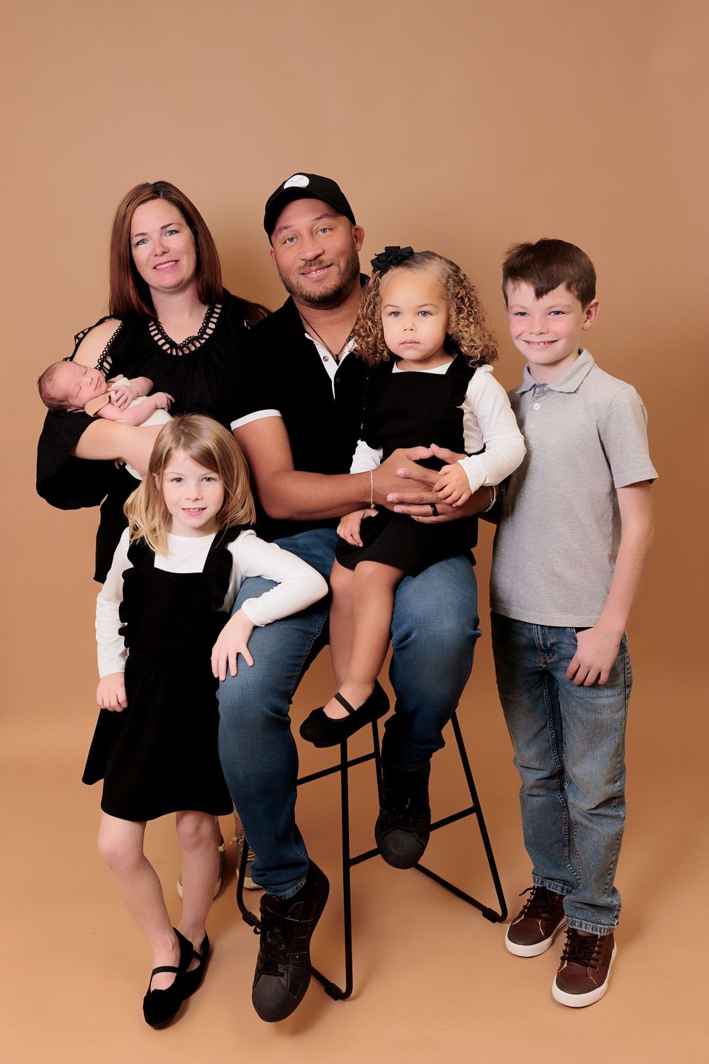 Studio family portrait with children and parents against warm brown backdrop.