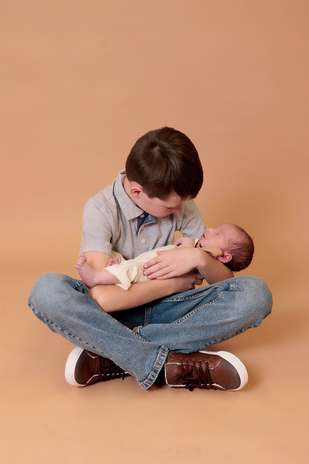 Young sibling tenderly holding newborn baby while sitting cross-legged.