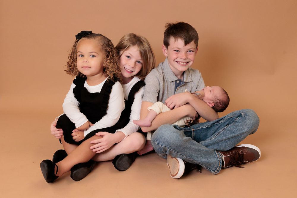 Siblings sitting together on brown backdrop during studio photoshoot.
