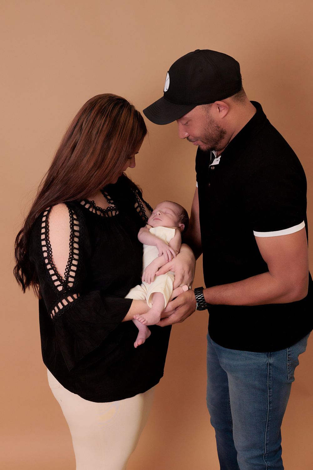 Parents gazing lovingly at their newborn baby against warm brown studio backdrop.