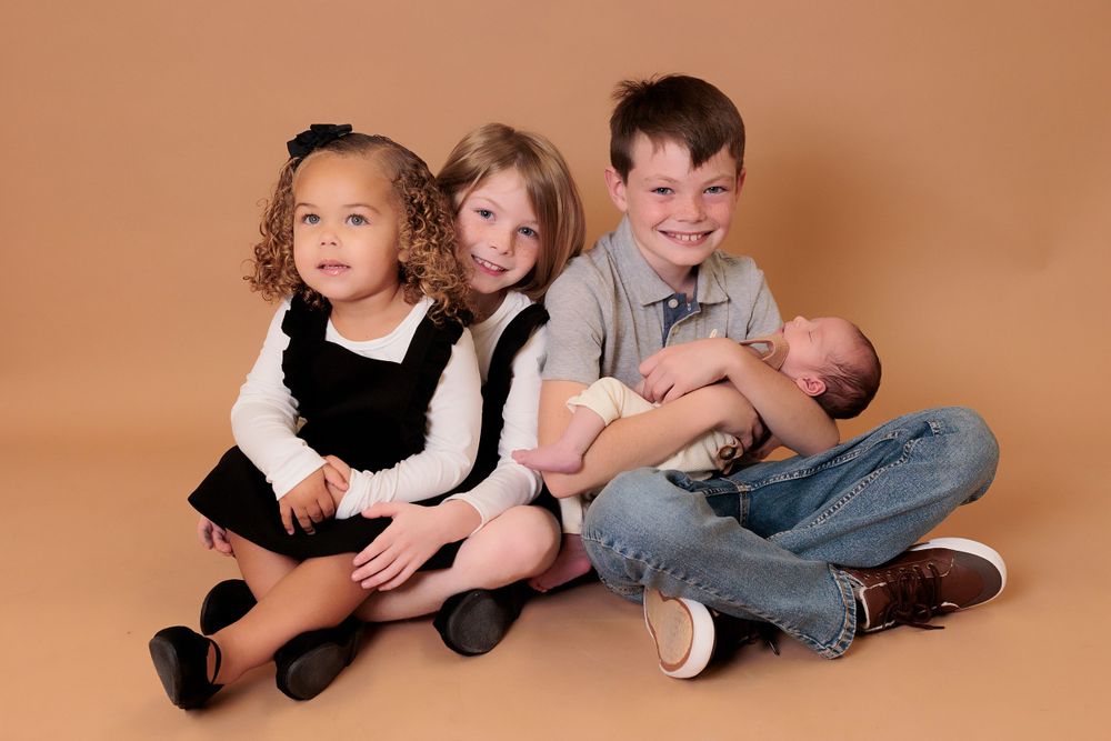 Three siblings posed together during professional photo session on brown backdrop.
