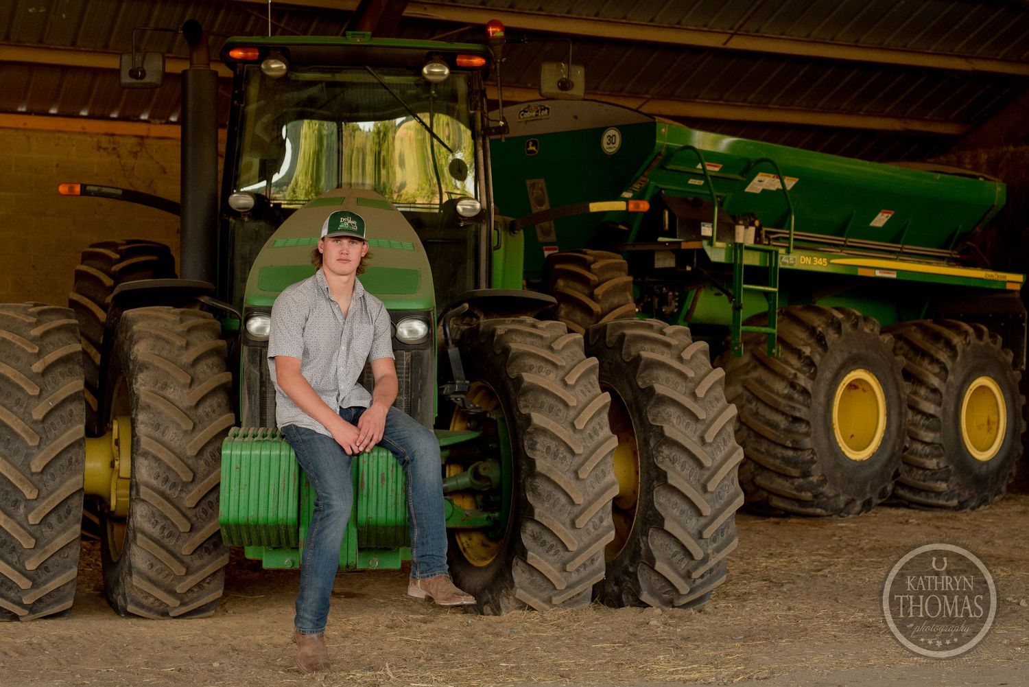 Farmer poses on large green tractor among multiple farm machines in covered storage area.