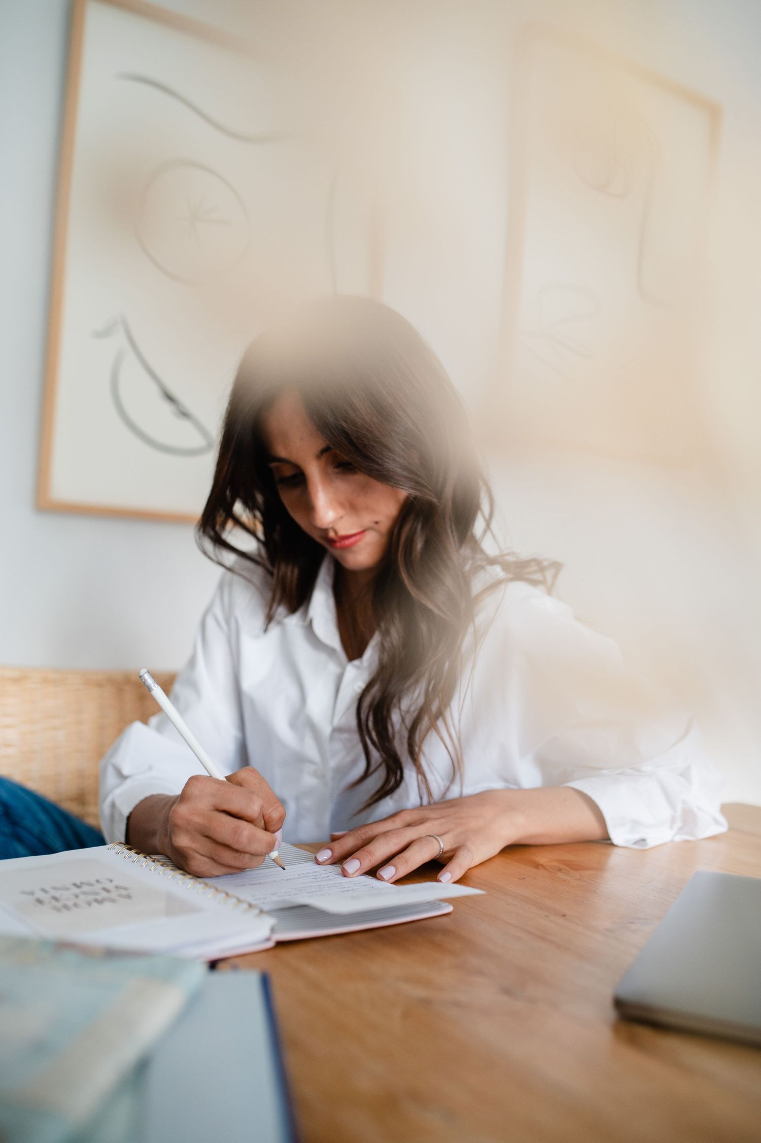 A person writes in a notebook while sitting at a wooden desk with natural lighting.