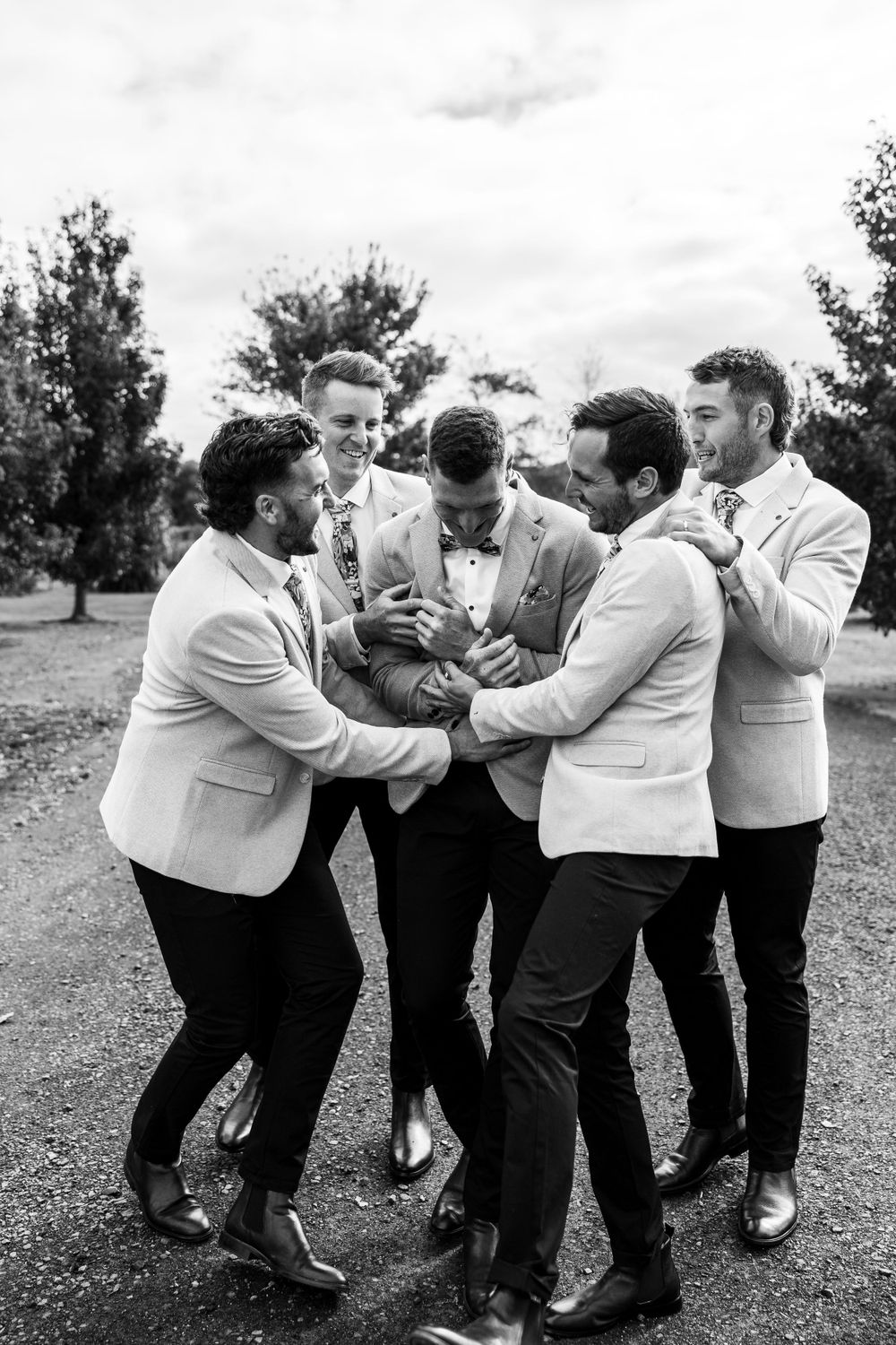 Wedding party in light suits playfully posing together in black and white photography.