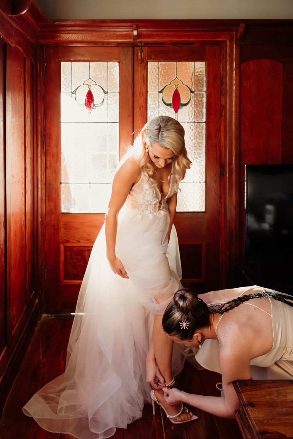 Wedding preparation scene in warm wooden room with white dress details.