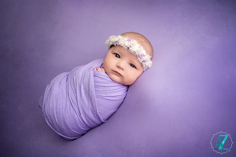 Sweet newborn portrait with purple wrap and delicate flower crown.
