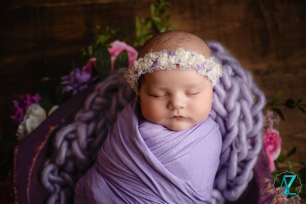 Close-up of sleeping baby in purple swaddle with delicate headband.