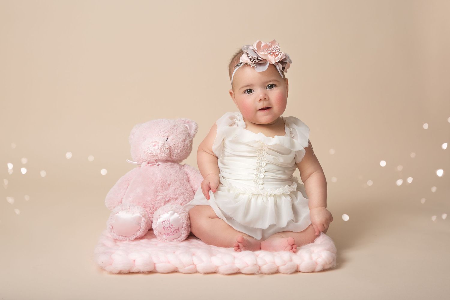 Sweet newborn photography series with baby in white dress and pink decorative elements against light background.