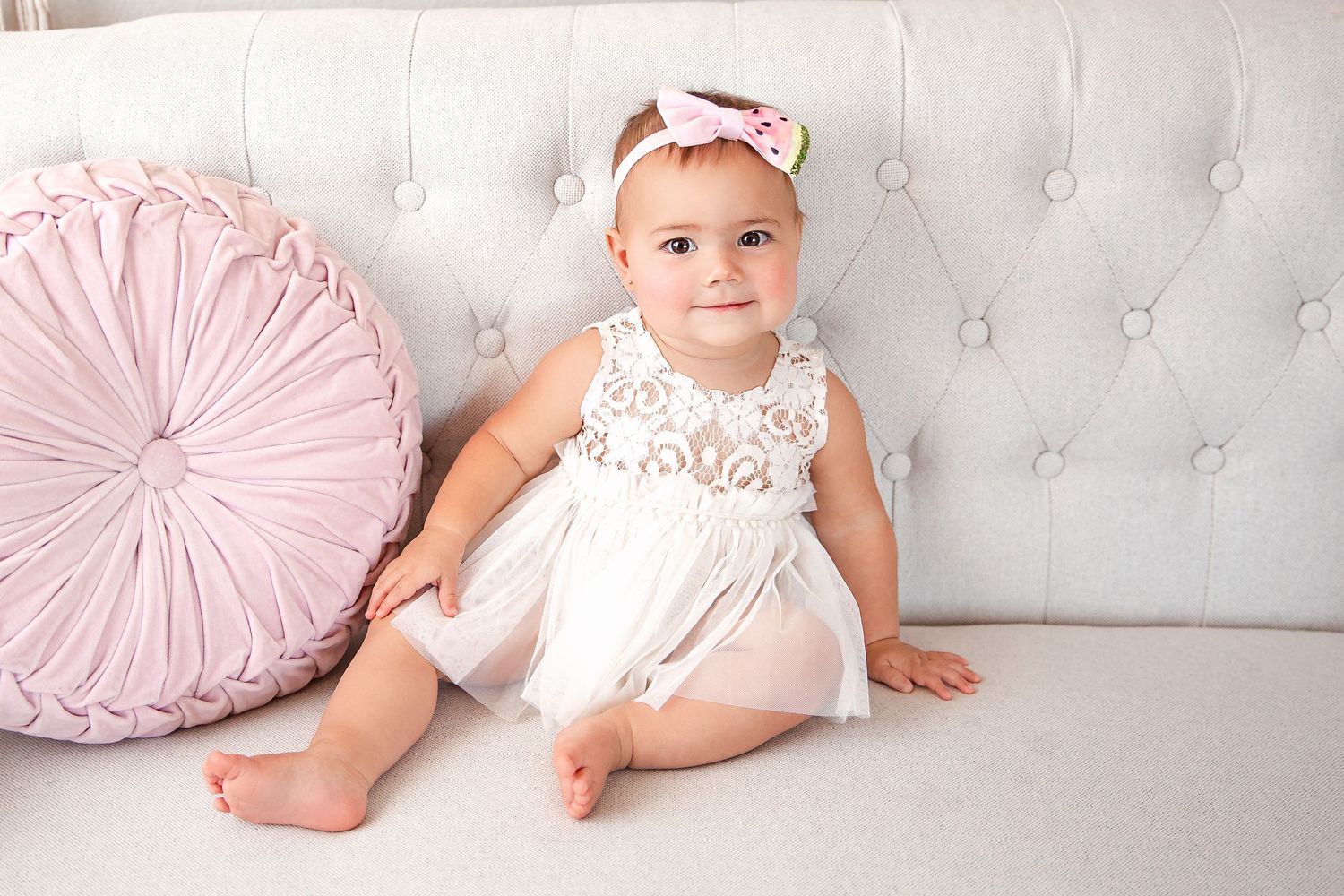 Baby portrait on white tufted couch with pink heart pillow and lace outfit.