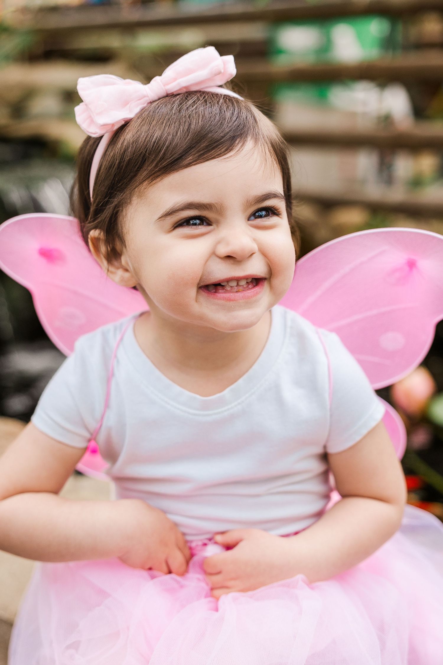 Young child wearing pink fairy wings and tutu smiles brightly outdoors.