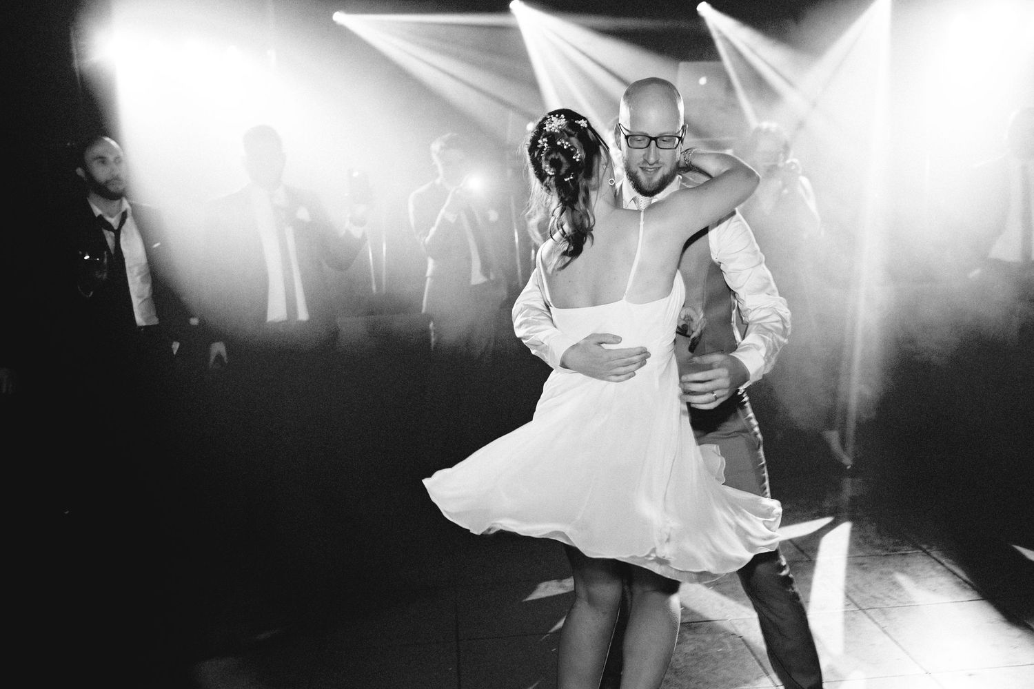 A couple spins dramatically on the dance floor under dramatic spotlight beams.