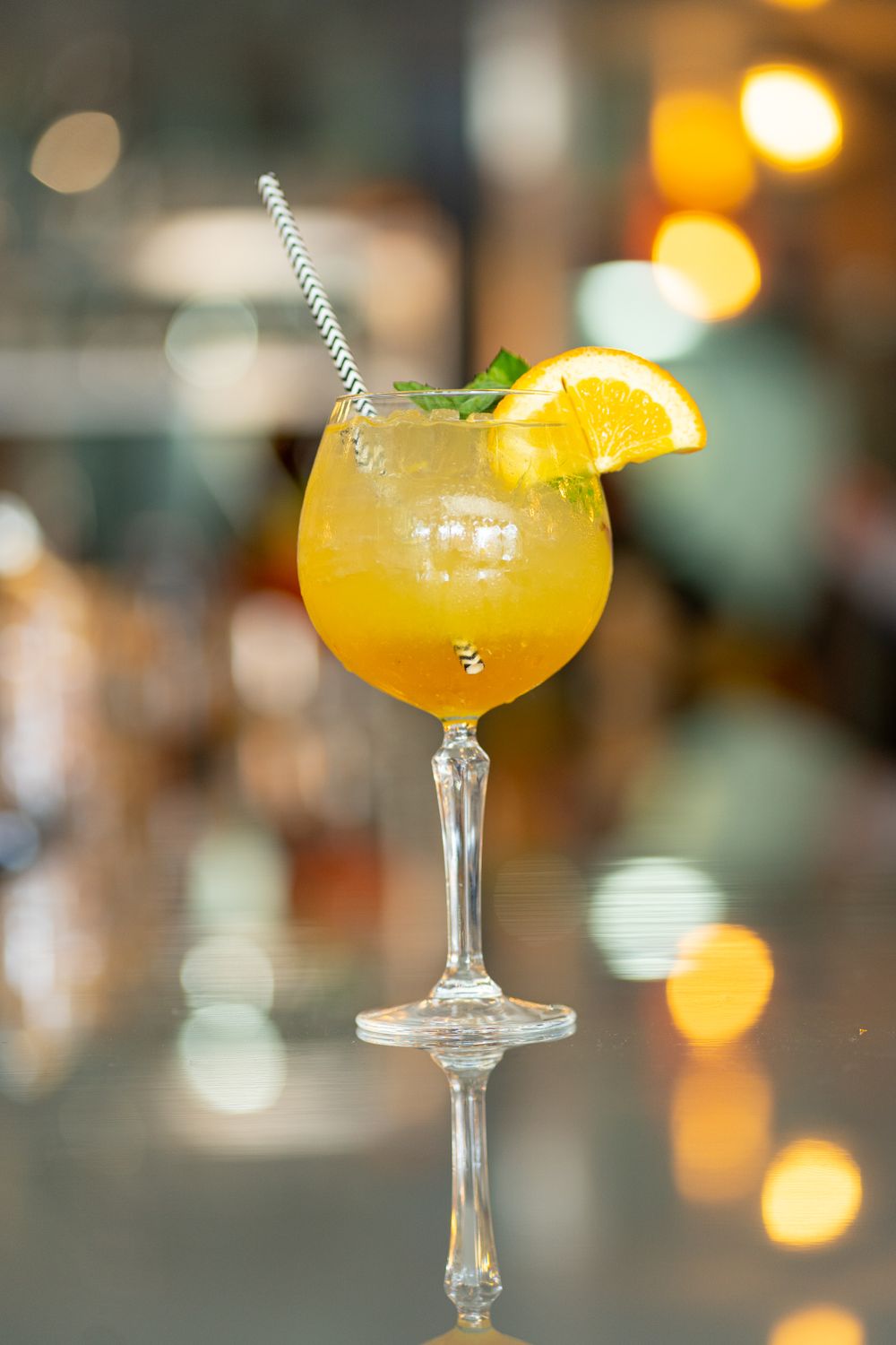 Michigan Commercial Photographer captures Orange cocktail garnished with citrus slice in elegant stemmed glass with bokeh background.