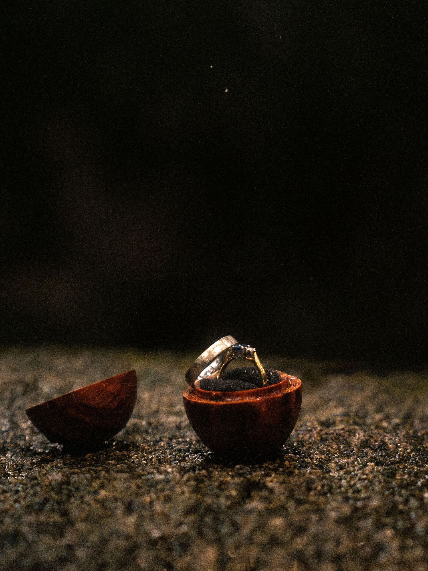 Wedding rings resting on dark textured surface with dramatic lighting.