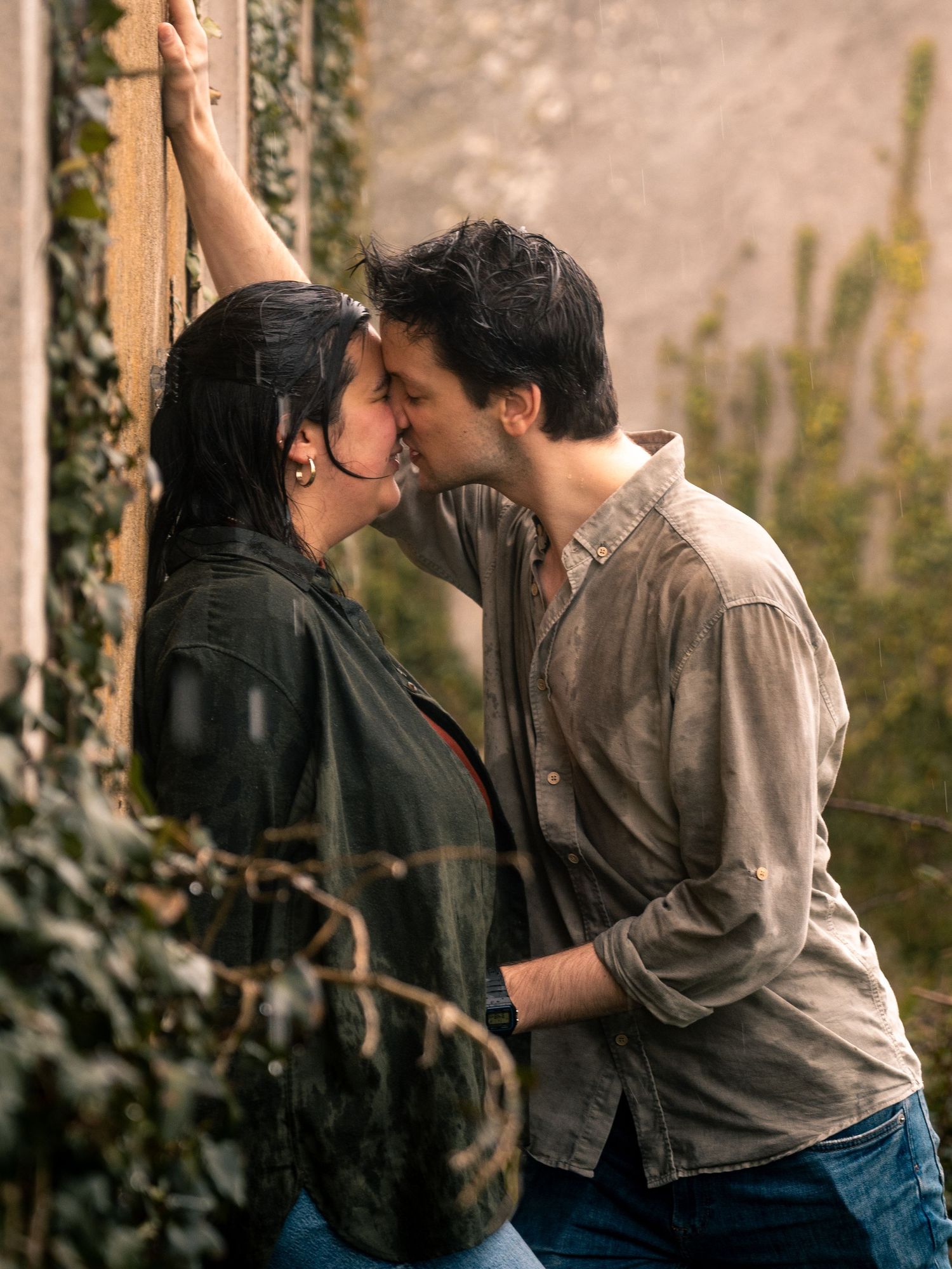 Couple in casual wear sharing romantic moment against rustic wall with ivy.