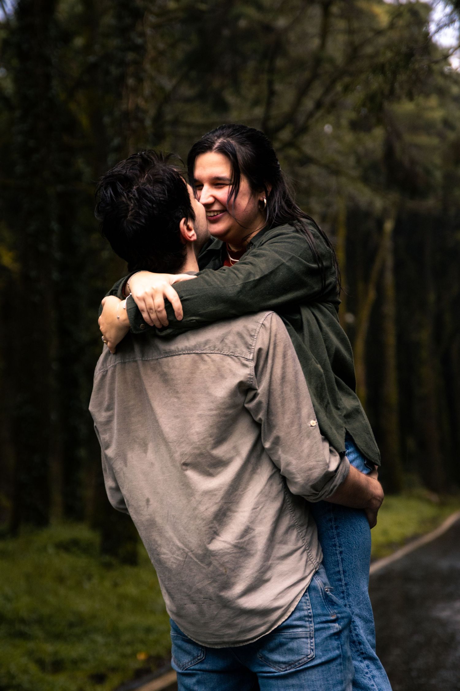 Two people hugging in forest wearing casual denim and grey clothing.