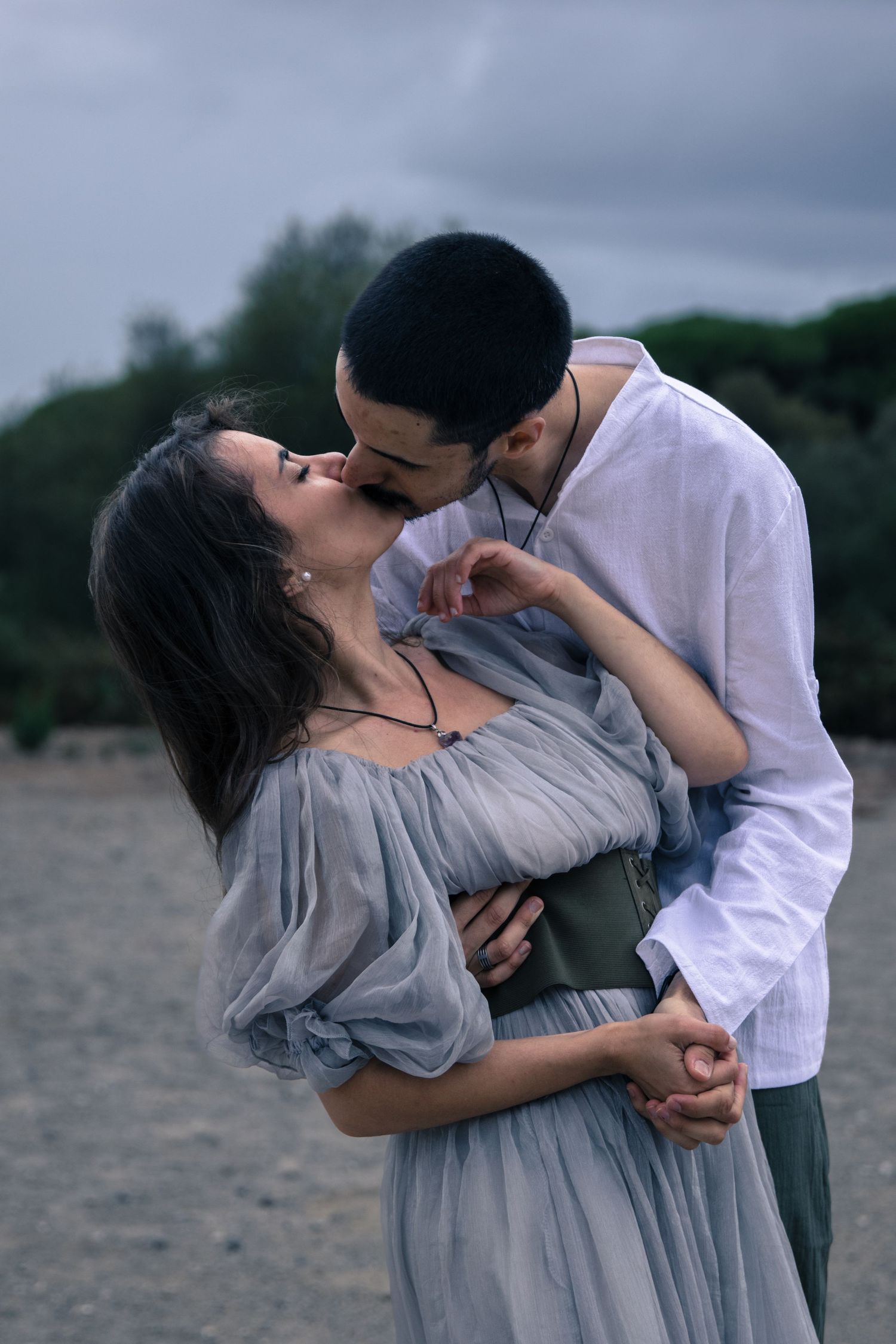 Romantic couple in intimate embrace wearing grey and white clothing on cloudy beach.