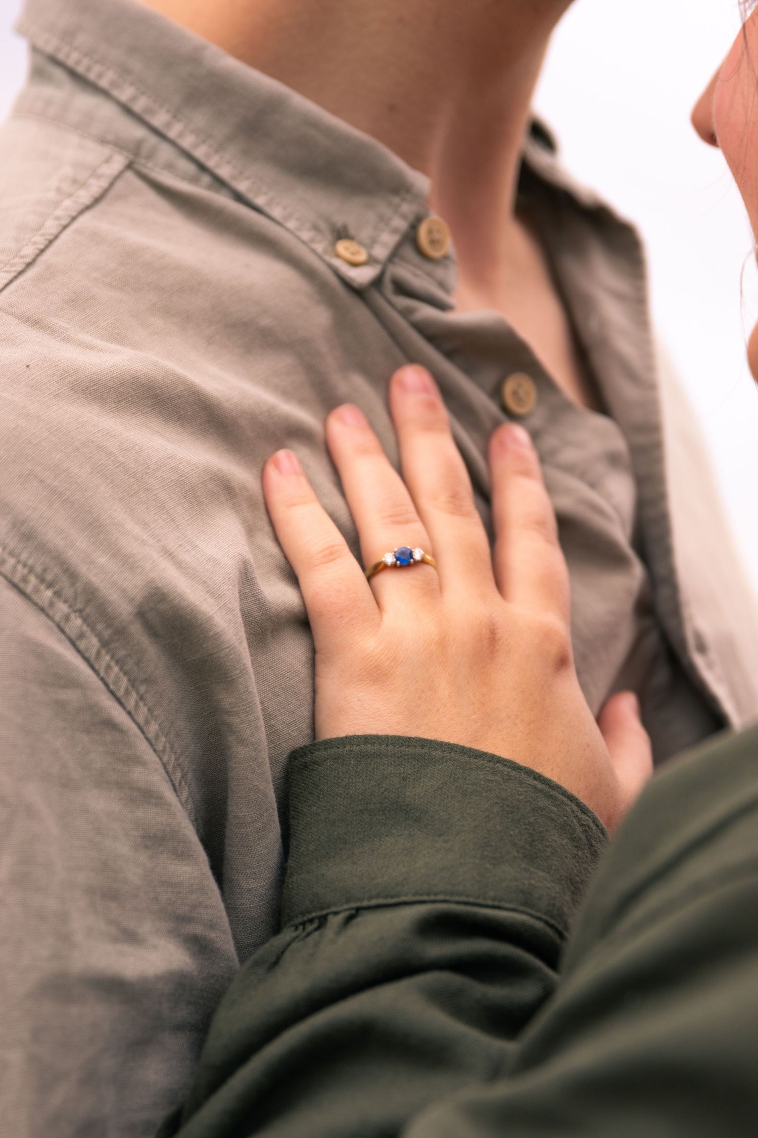 Close up of hands resting on grey fabric with a ring visible.