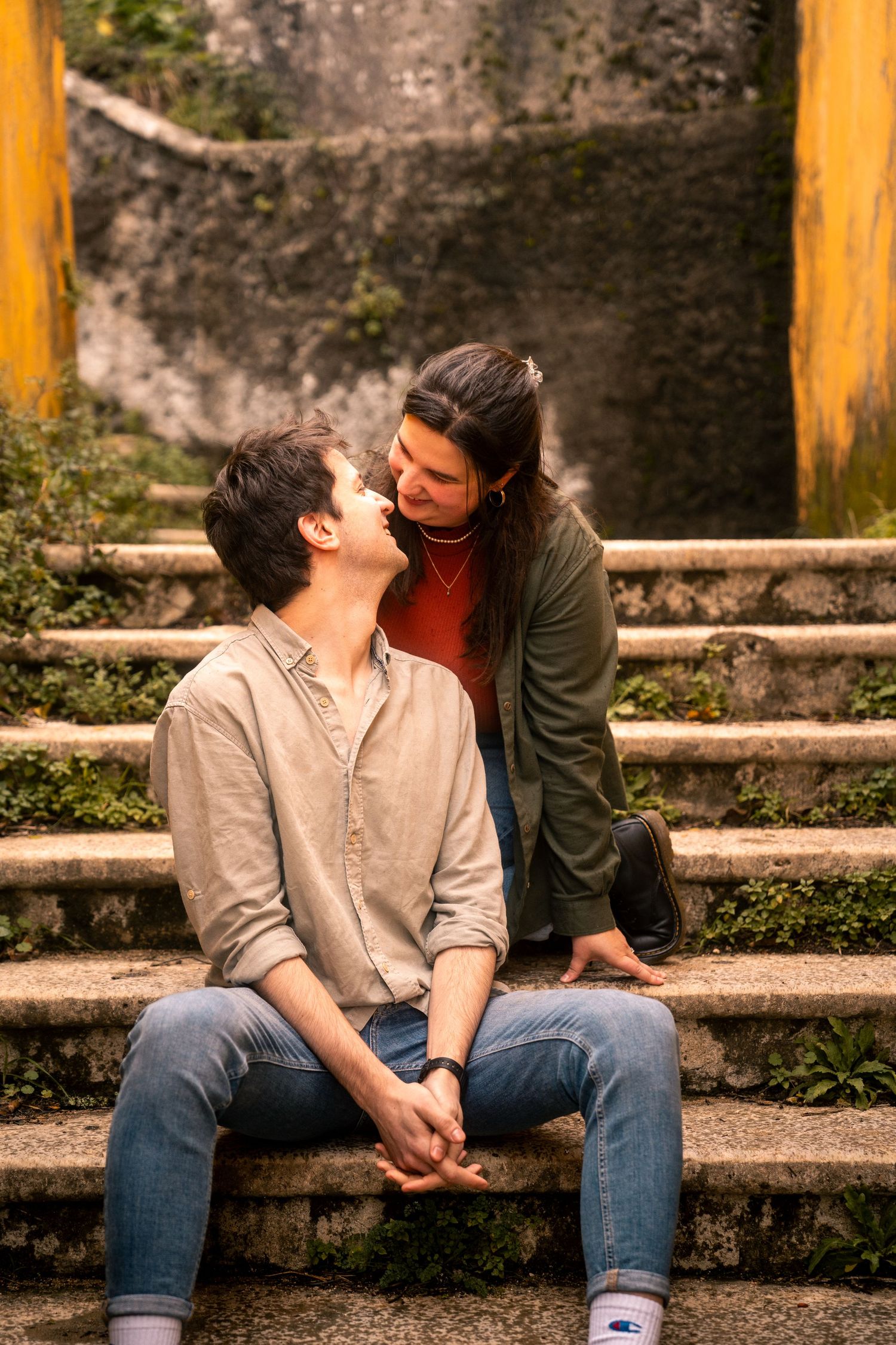 Two people sharing intimate moment on concrete steps with yellow wall background.