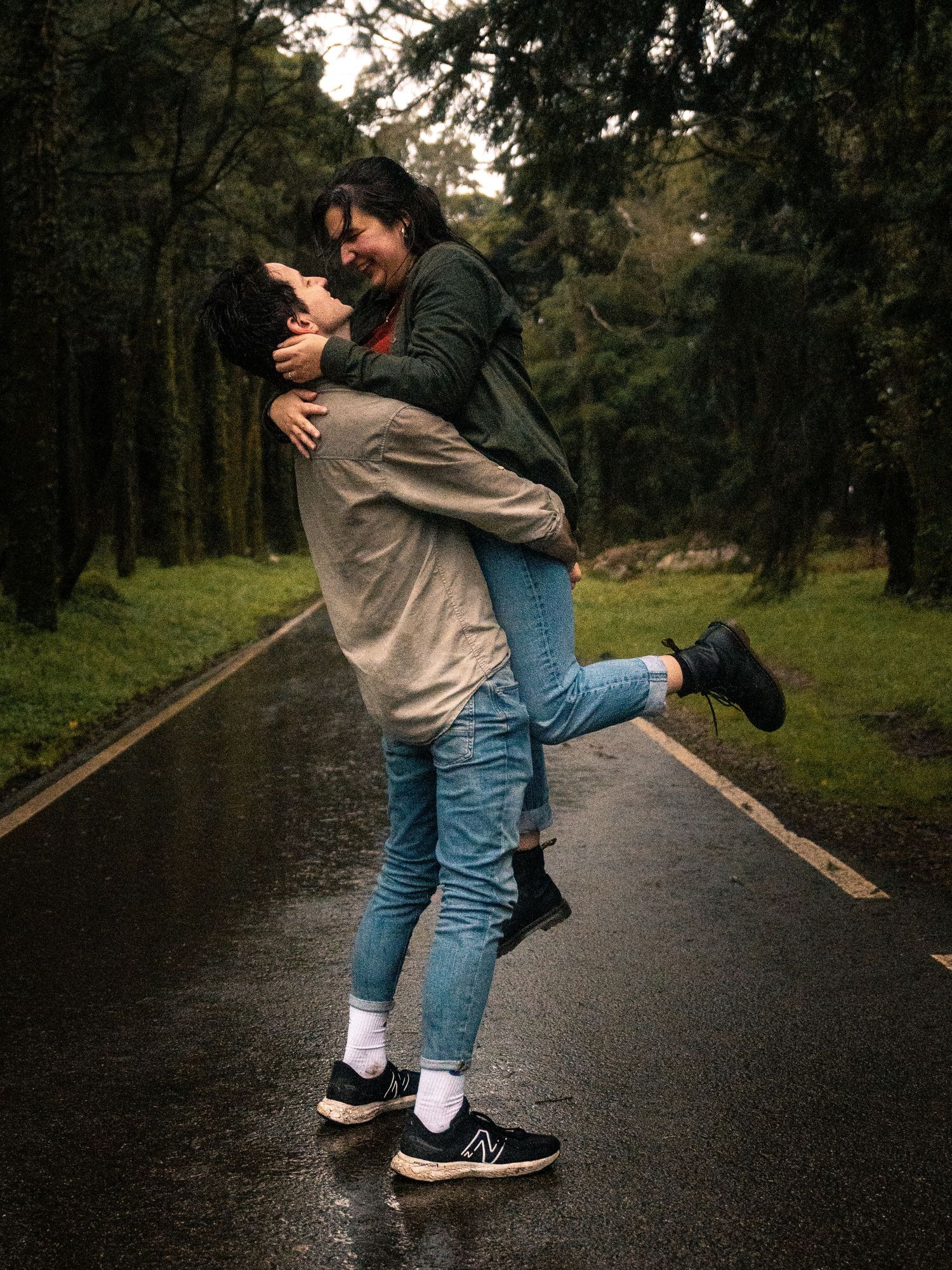 Romantic embrace on a wet path surrounded by green trees.