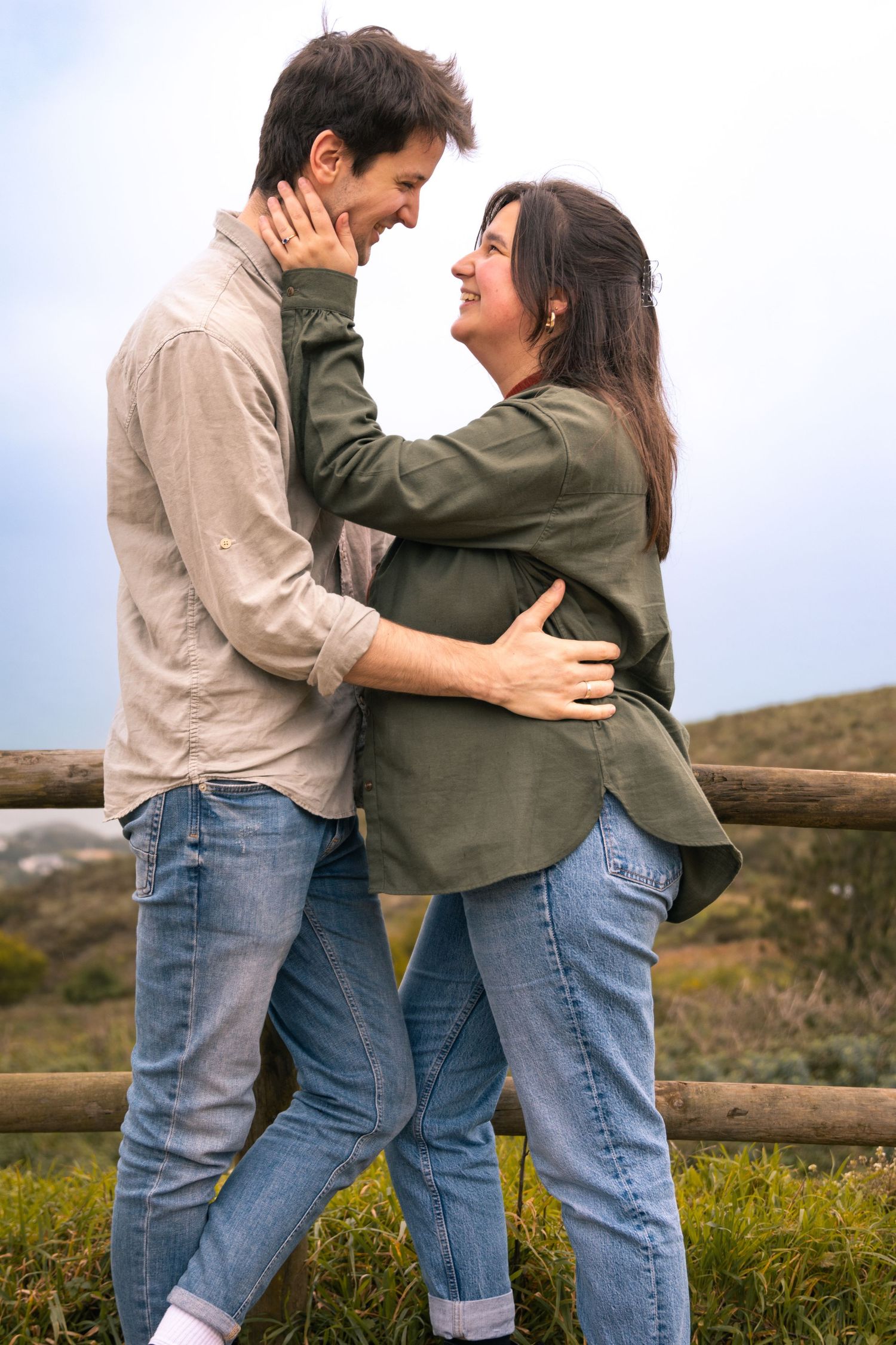 Couple in casual wear embracing on a wooden fence in countryside setting.