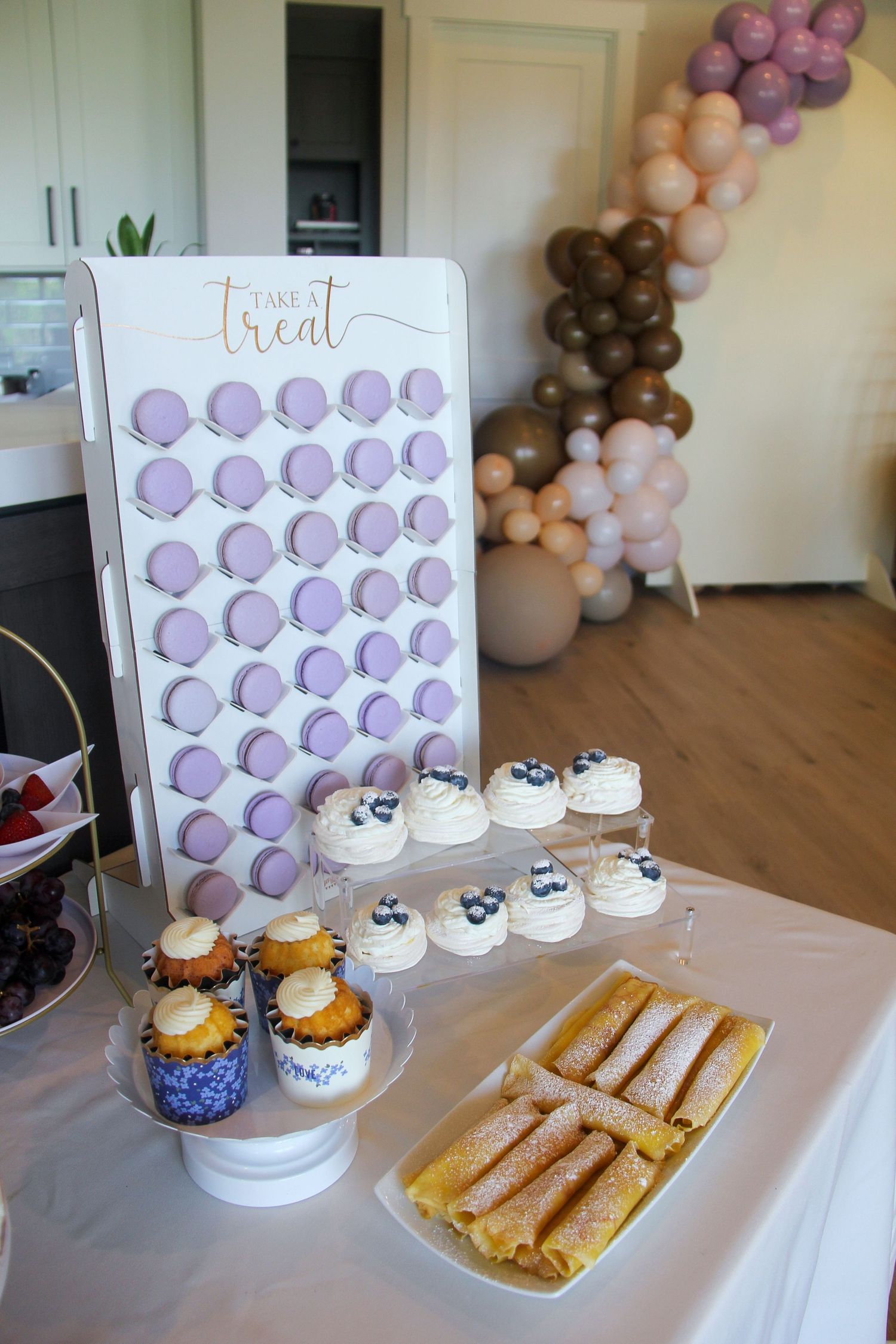 lilac baby shower dessert table with macaroons, cupcakes, crepes, and balloon backdrop