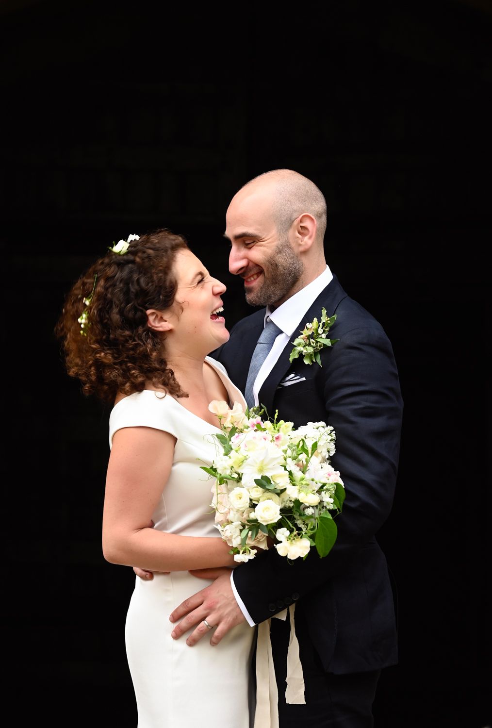 Intimate portrait of couple with white floral bouquet against black background.