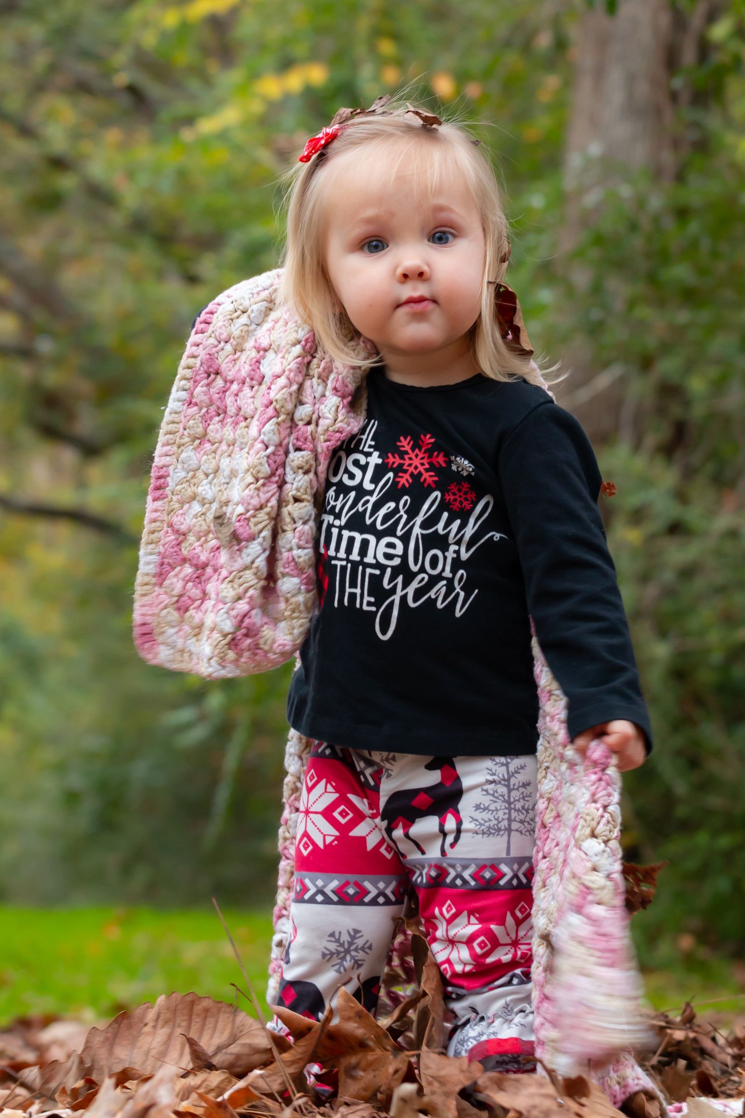 Young child in festive winter outfit sitting among fallen autumn leaves.