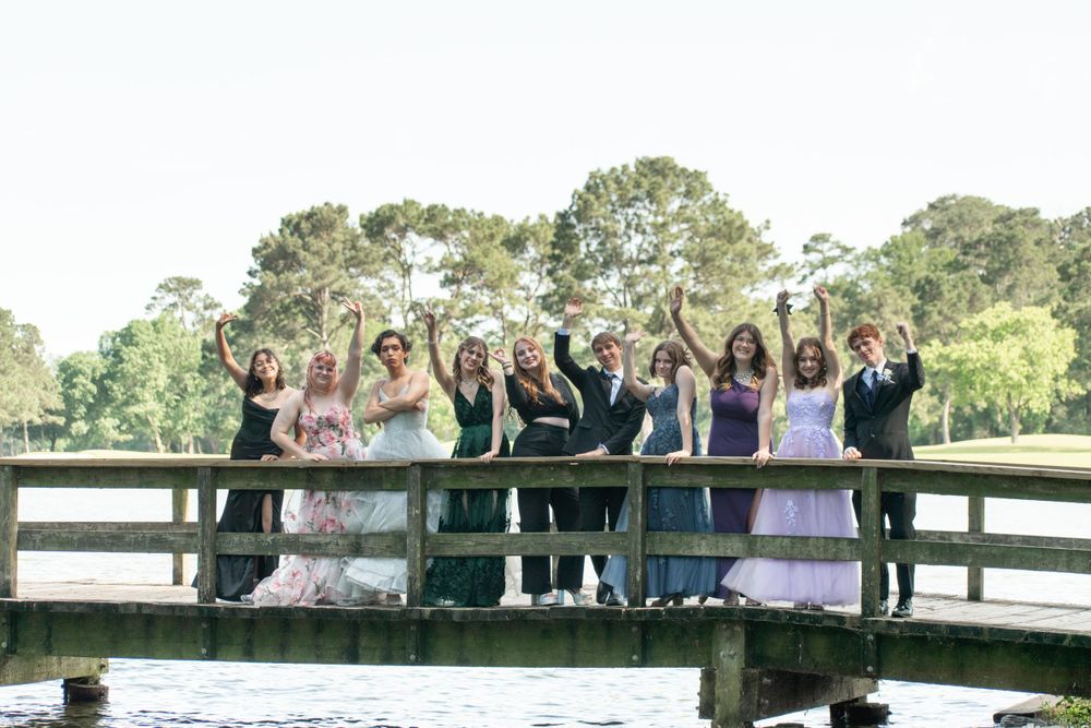 Wedding party celebrating on a wooden bridge over water surrounded by trees in an outdoor setting.