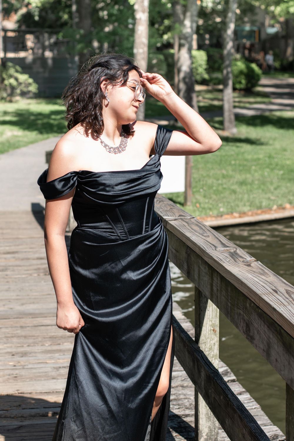Woman in black velvet formal dress poses dramatically on wooden boardwalk.