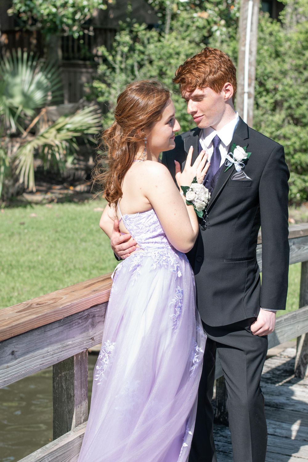 Couple in formal attire share an intimate moment on a wooden deck during prom or wedding photoshoot.