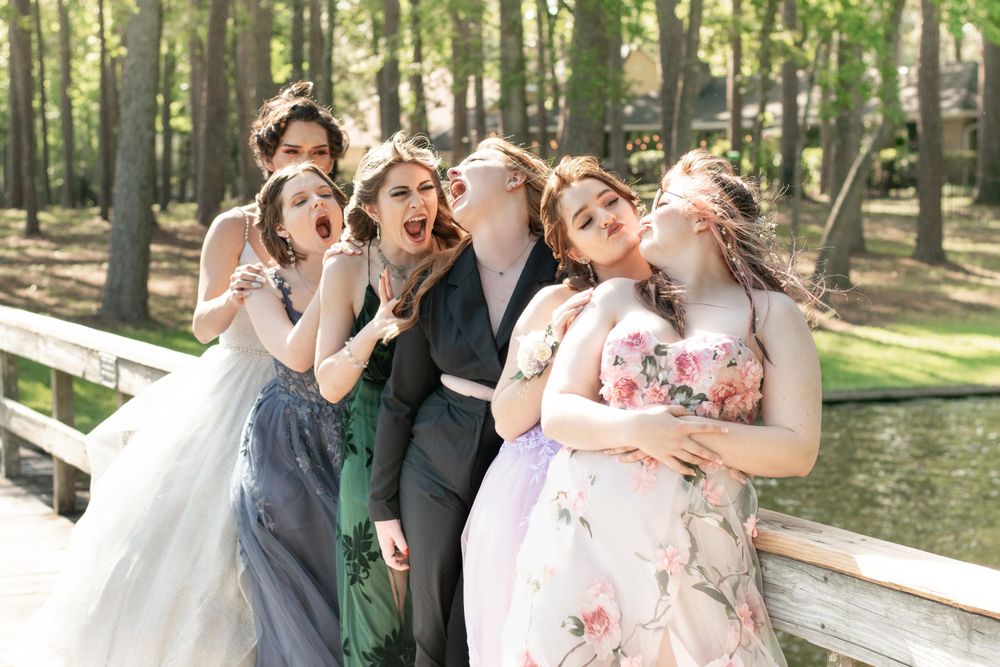 Wedding party making silly faces and poses on a wooden bridge in a forest setting.