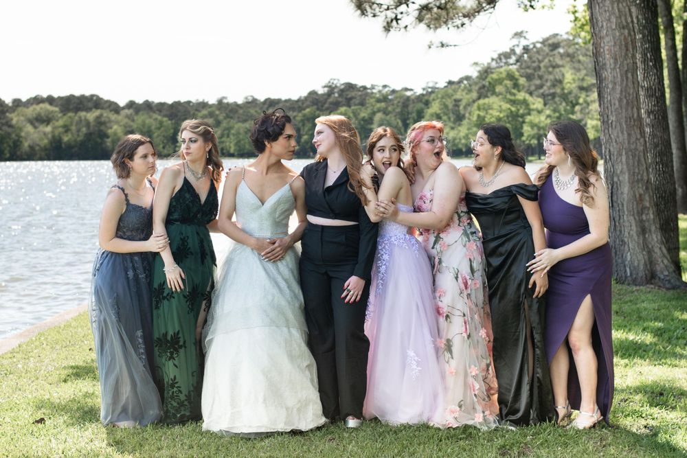 Group in formal attire posing by a lake with trees in the background.