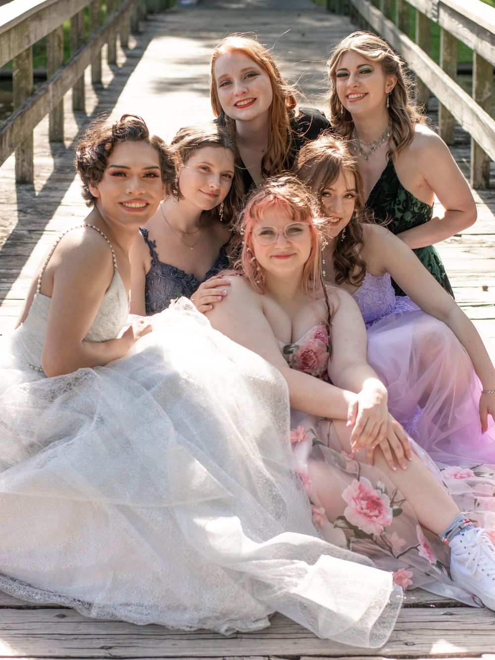 Friends in formal attire pose together on wooden boardwalk in evening light.