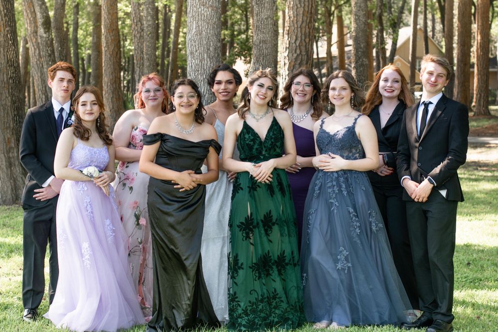 Formal group photo of prom or wedding party wearing elegant dresses in forest setting.