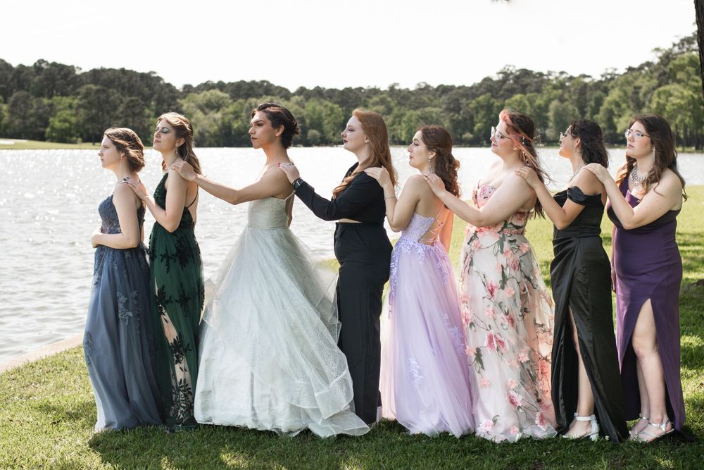 Elegant group photo of wedding party in flowing dresses posed by lakeside.