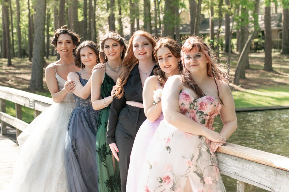 Bridal party in mix of formal dresses posing together on wooden bridge in forest setting.